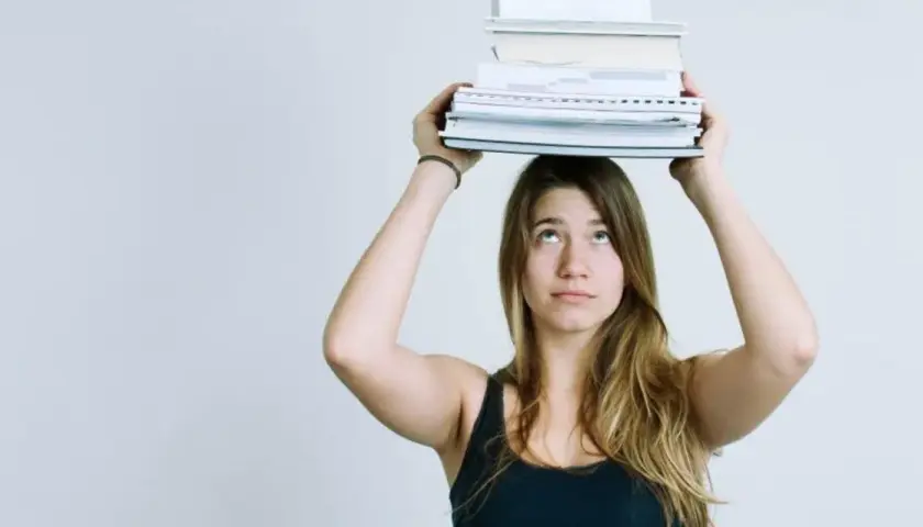 Junge Frau balanciert Bücher auf dem Kopf. Das Gewicht symbolisiert den Lernaufwand im Gymnasium und die Herausforderung des strukturierten Lernens.