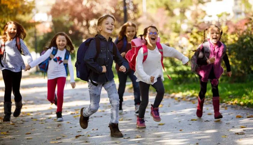 Fröhliche Grundschüler mit Rucksäcken rennen auf dem Schulweg nach den Ferien.