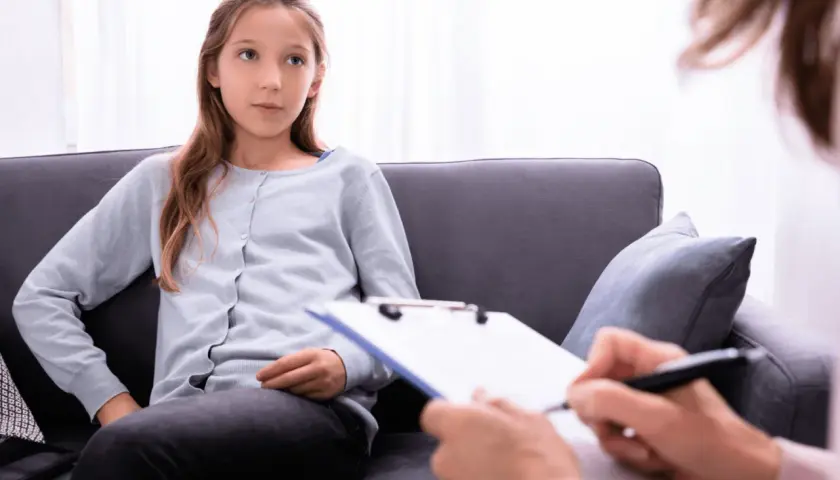 Ein Mädchen sitzt auf einer Couch und spricht mit einer Person, die Notizen macht. Die Frage, ob ADHS heilbar ist, wird hier thematisiert.