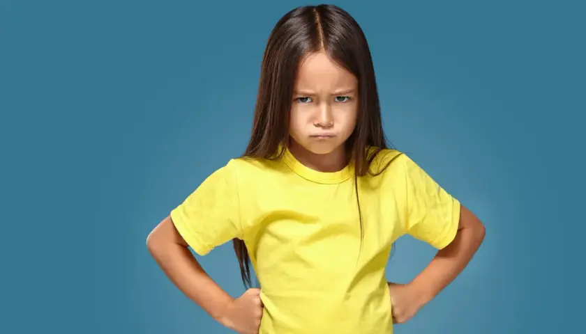 Ein kleines Mädchen mit ernstem Gesichtsausdruck und Händen in den Hüften, das aggressives Verhalten bei Kindern im Kindergarten zeigt.