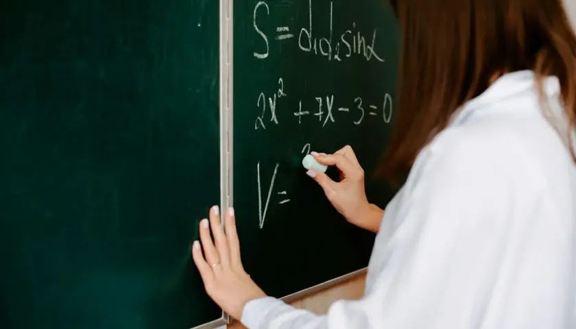 Eine Hand schreibt mit Kreide Formeln an eine Tafel. So kann man Mathe besser verstehen und komplexe Gleichungen lösen.