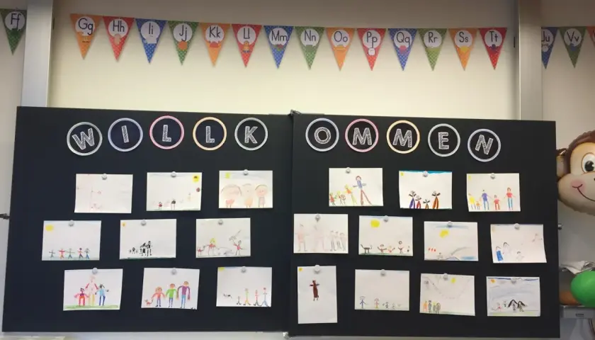 Willkommen zur 1. Klasse! Kinderzeichnungen schmücken die Tafel, ein bunter ABC-Girlande hängt darüber.