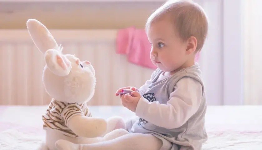 Ein Baby spielt mit einem Stoffhasen. Die Augen des Babys sind auf den Hasen gerichtet, was auf frühe Anzeichen von Autismus hindeuten könnte.