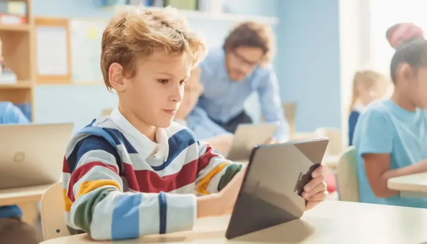 Schüler lernen mit Tablets und Laptops im Klassenzimmer. Ein Lehrer unterstützt sie. Dies ist ein Beispiel für den DigitalPakt 2.0.