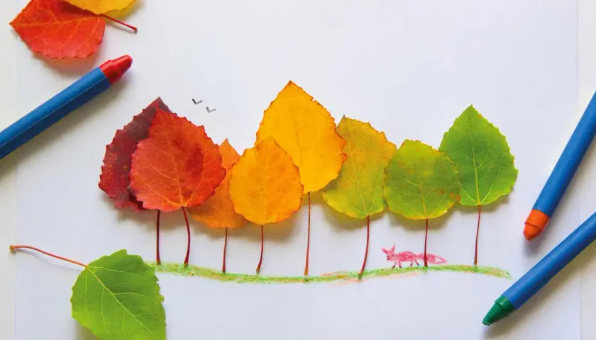 Bunte Blätter bilden Bäume, ein kleiner Fuchs spaziert im Herbst im Kindergarten. Buntstifte liegen daneben.