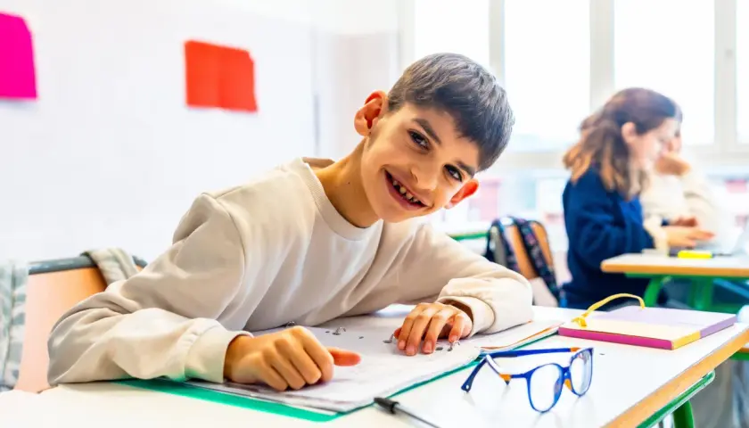 Ein lächelnder Junge lernt in einem Klassenzimmer. Dies ist ein Beispiel für **Inklusion an Schulen**, wo alle Kinder gemeinsam lernen und wachsen.