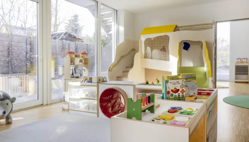 Ein heller, freundlicher gruppenraum raumgestaltung kita ideen mit Spielturm, Rutsche, Spielküche und vielen Spielsachen.