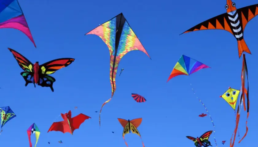 Bunte Drachen in Form von Schmetterlingen, Fledermäusen und geometrischen Mustern steigen im blauen Himmel auf. Ein Fest des Drachenbastelns!