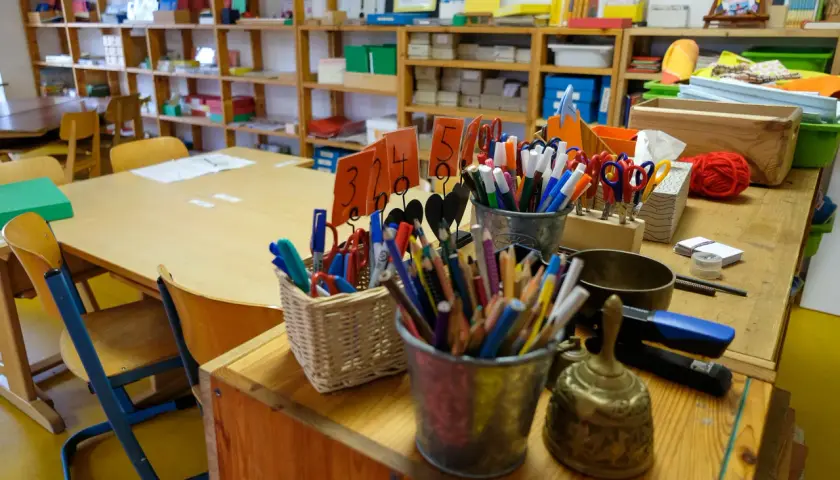 Buntstifte, Scheren und ein Gong auf einem Tisch in einer Montessori-Schule. Die Kosten für eine Montessori-Schule können variieren.