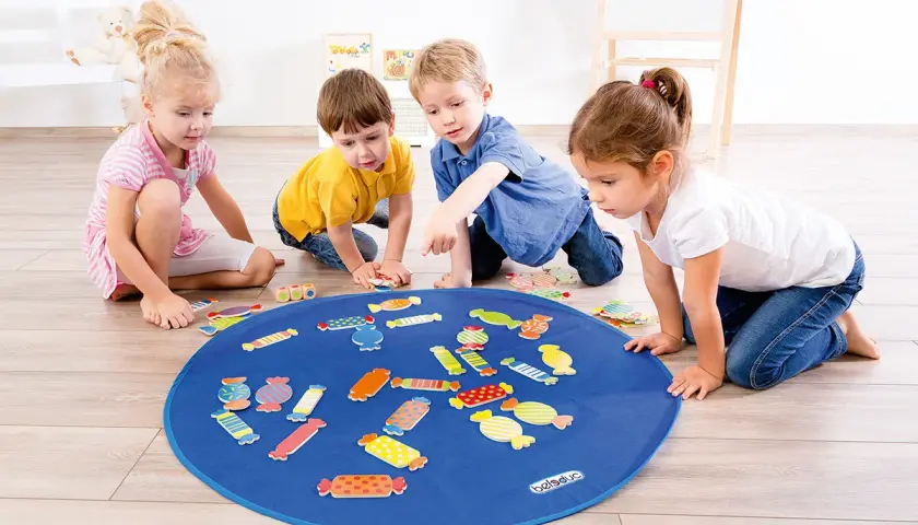 Vier Kinder spielen mit bunten Bonbon-Formen auf einer blauen Matte. Tolle Kindergarten spiele für kleine Entdecker.