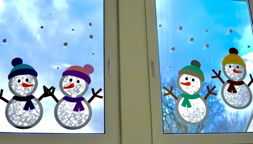 Süße Schneemann-Fensterdeko basteln mit Kindern. Vier fröhliche Schneemänner mit bunten Mützen und Schals zieren das Fenster.