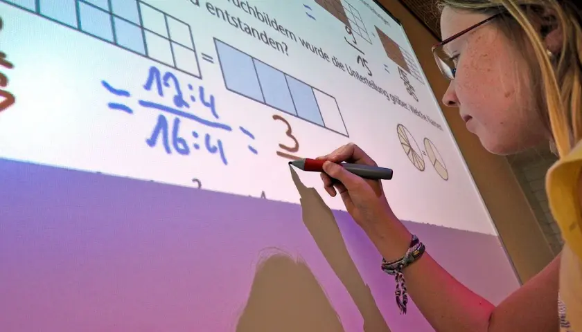 Ein Mädchen schreibt auf einem interaktiven Whiteboard, das Matheaufgaben zeigt. Solche Whiteboards sind moderne Tafeln für den Unterricht.