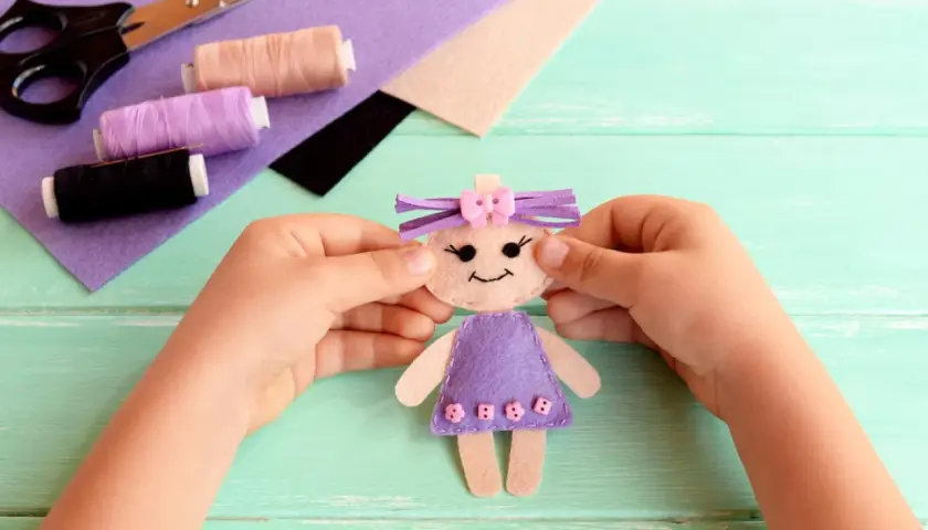 Kleine Hände basteln eine Filzpuppe. Schere, Faden und Filz liegen bereit für das Filzen mit Kindern.