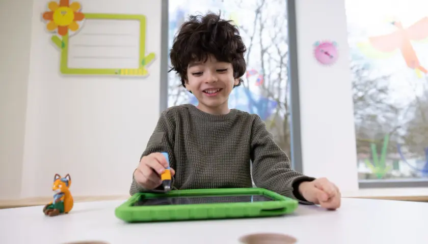 Ein Junge übt mit einem Stift auf einem Tablet, was eine spielerische Art ist, graphomotorische Fähigkeiten zu entwickeln.