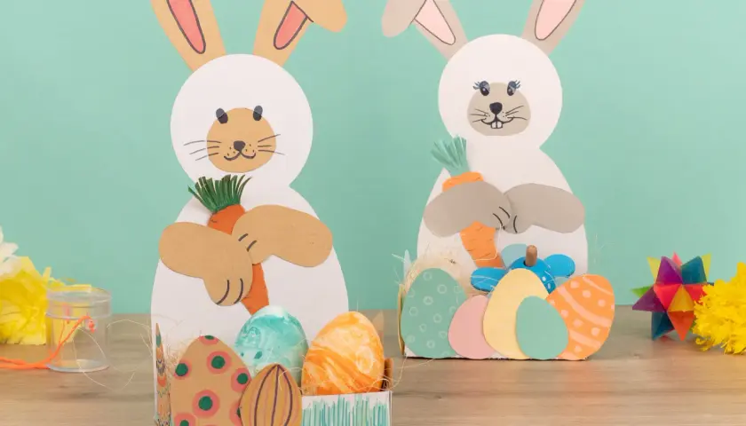 Zwei süße Osterhasen zum osterhase basteln halten Karotten. Bunte Ostereier liegen in Körbchen.