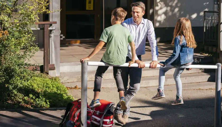 Ein Mann spricht mit zwei Kindern vor einer Schule. Vielleicht plant er, als lehrer bundesland wechseln.