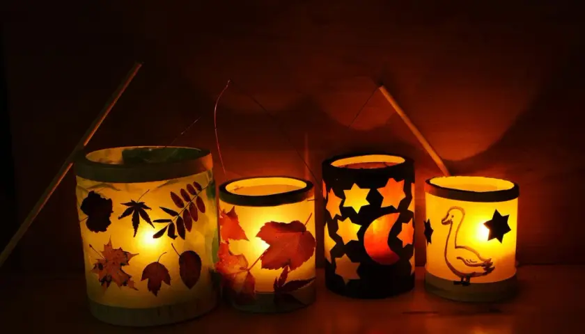 Vier selbstgebastelte Tischlaternen für Kinder leuchten warm. Mit Blättern, Sternen, Mond und einem Gänse-Motiv.