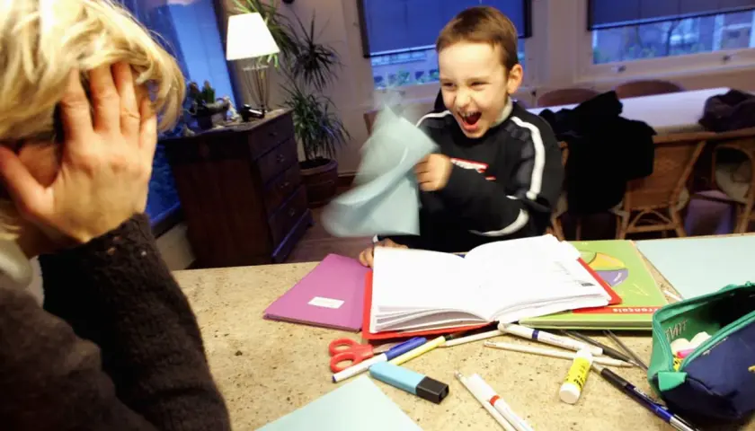 Ein Junge mit ADHS wirft Papier, während seine Mutter verzweifelt die Hände vors Gesicht schlägt.