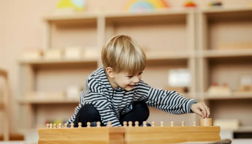 Ein Junge spielt konzentriert mit Holzbausteinen in einem Montessori Kindergarten.