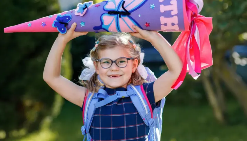 Ein Mädchen mit Schultüte und Rucksack, bereit für die erste Klasse Grundschule. Bunte Schmetterlinge zieren die Schultüte.