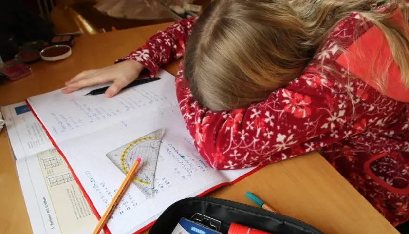 Müdes Kind mit Kopf auf dem Schreibtisch, umgeben von Schulbüchern und Stiften. Vielleicht helfen Ritalin Tabletten bei der Konzentration?