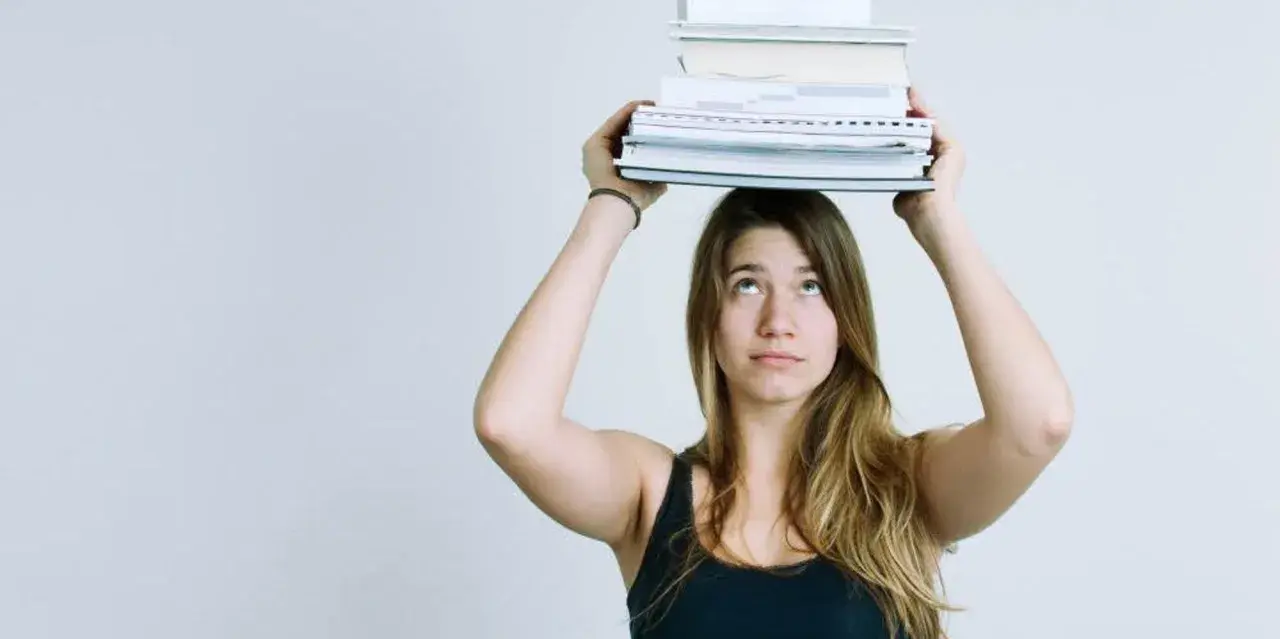 Junge Frau balanciert Bücher auf dem Kopf. Das Gewicht symbolisiert den Lernaufwand im Gymnasium und die Herausforderung des strukturierten Lernens.