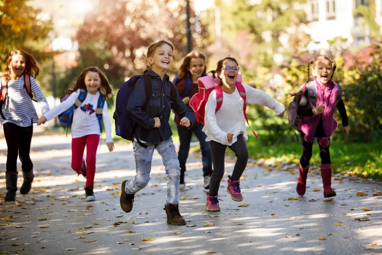 Fröhliche Grundschüler mit Rucksäcken rennen auf dem Schulweg nach den Ferien.