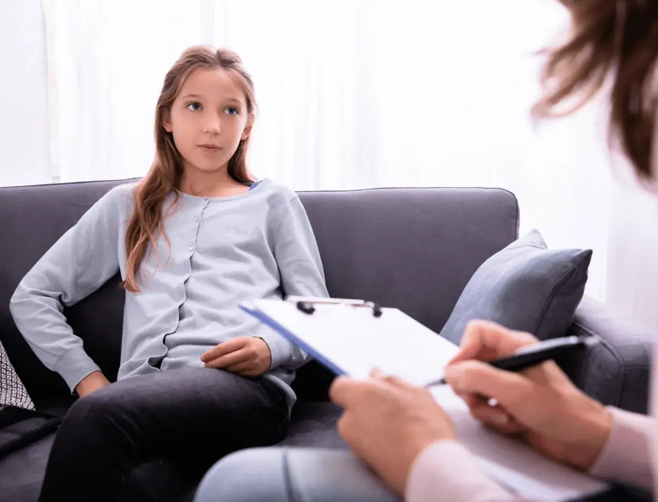 Ein Mädchen sitzt auf einer Couch und spricht mit einer Person, die Notizen macht. Die Frage, ob ADHS heilbar ist, wird hier thematisiert.