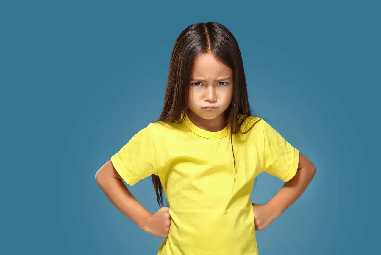 Ein kleines Mädchen mit ernstem Gesichtsausdruck und Händen in den Hüften, das aggressives Verhalten bei Kindern im Kindergarten zeigt.