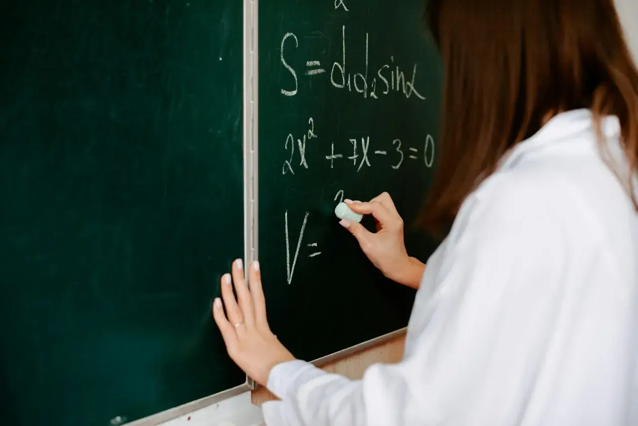Eine Hand schreibt mit Kreide Formeln an eine Tafel. So kann man Mathe besser verstehen und komplexe Gleichungen lösen.