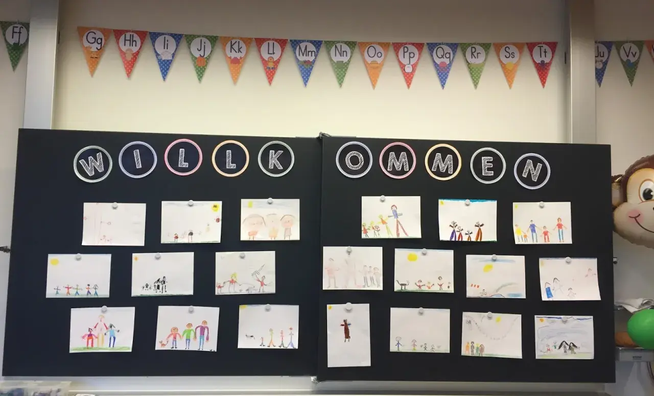 Willkommen zur 1. Klasse! Kinderzeichnungen schmücken die Tafel, ein bunter ABC-Girlande hängt darüber.