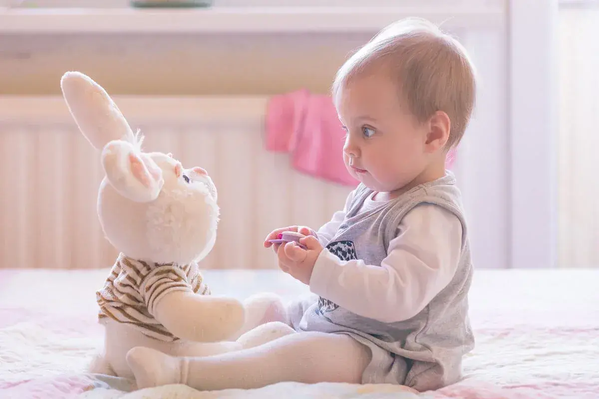 Ein Baby spielt mit einem Stoffhasen. Die Augen des Babys sind auf den Hasen gerichtet, was auf frühe Anzeichen von Autismus hindeuten könnte.