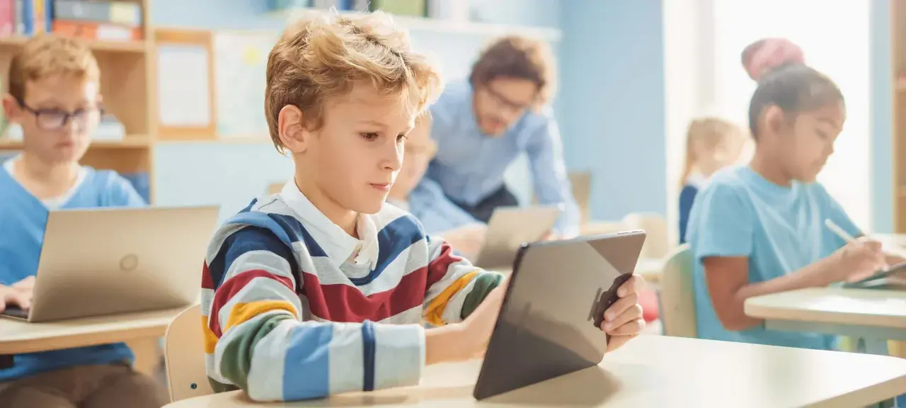 Schüler lernen mit Tablets und Laptops im Klassenzimmer. Ein Lehrer unterstützt sie. Dies ist ein Beispiel für den DigitalPakt 2.0.
