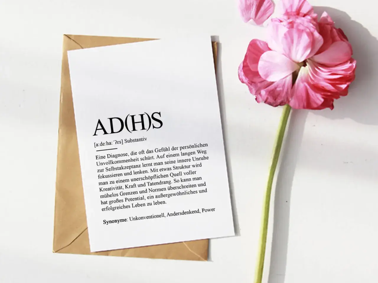 ADHS-Diagnostik online: Ein Blatt mit der Definition von ADHS liegt auf einem Umschlag, daneben eine rosa Blüte.