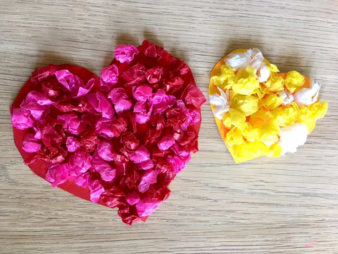 Zwei bunte Herzen, rot und gelb, mit zerknülltem Seidenpapier beklebt. Perfekt zum Herzen basteln mit Kindern!