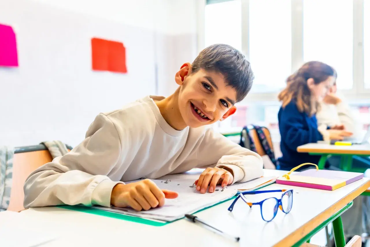 Ein lächelnder Junge lernt in einem Klassenzimmer. Dies ist ein Beispiel für **Inklusion an Schulen**, wo alle Kinder gemeinsam lernen und wachsen.