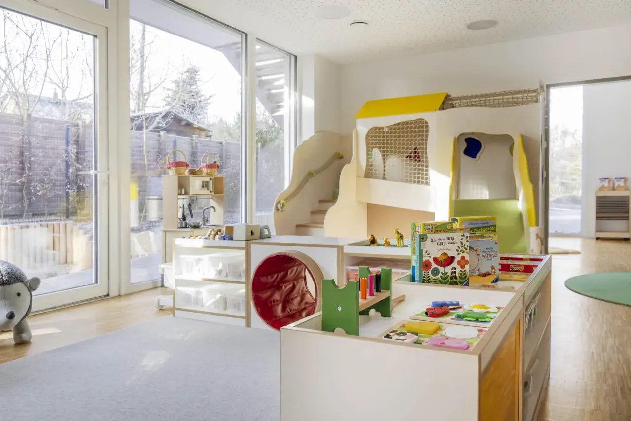 Ein heller, freundlicher gruppenraum raumgestaltung kita ideen mit Spielturm, Rutsche, Spielküche und vielen Spielsachen.