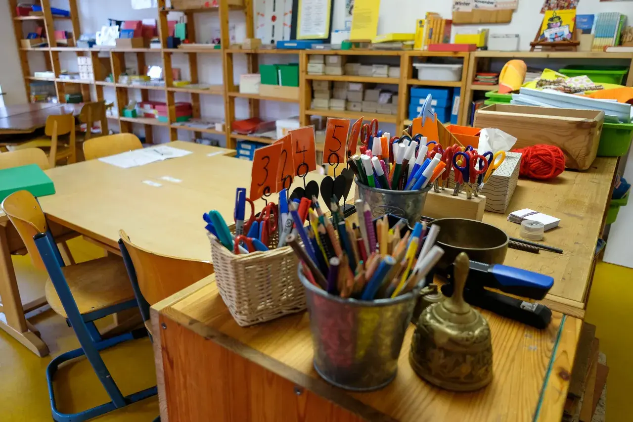 Buntstifte, Scheren und ein Gong auf einem Tisch in einer Montessori-Schule. Die Kosten für eine Montessori-Schule können variieren.