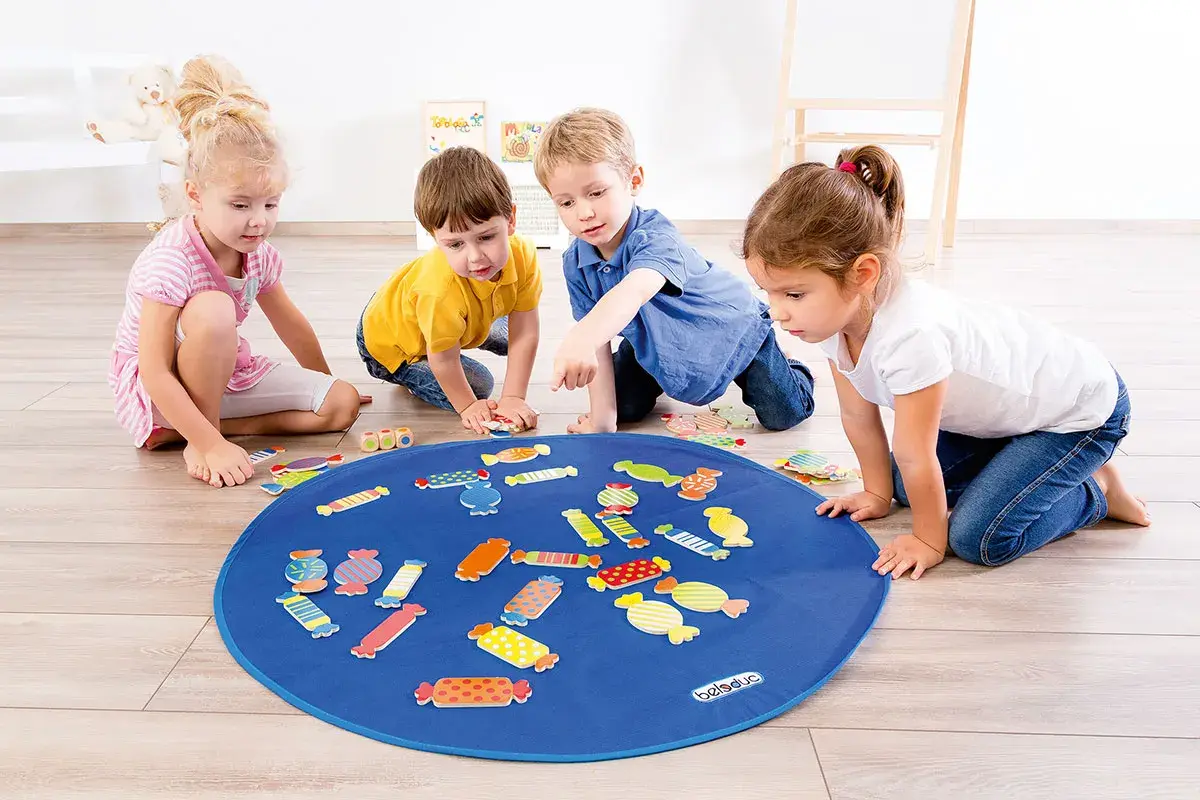 Vier Kinder spielen mit bunten Bonbon-Formen auf einer blauen Matte. Tolle Kindergarten spiele für kleine Entdecker.