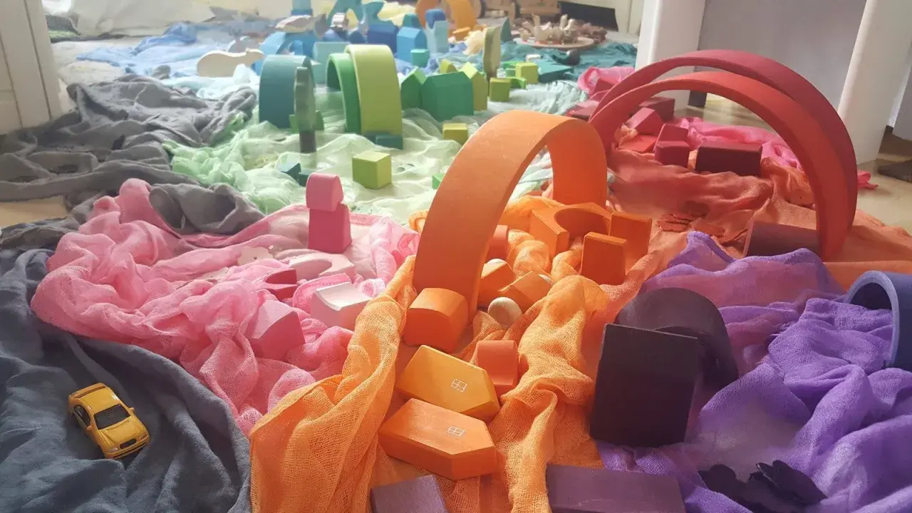 Bunte Stoffe und Holzbausteine, die an eine Regenbogenstadt erinnern. Perfekt für einen kreativen Kindergartenbericht schreiben.