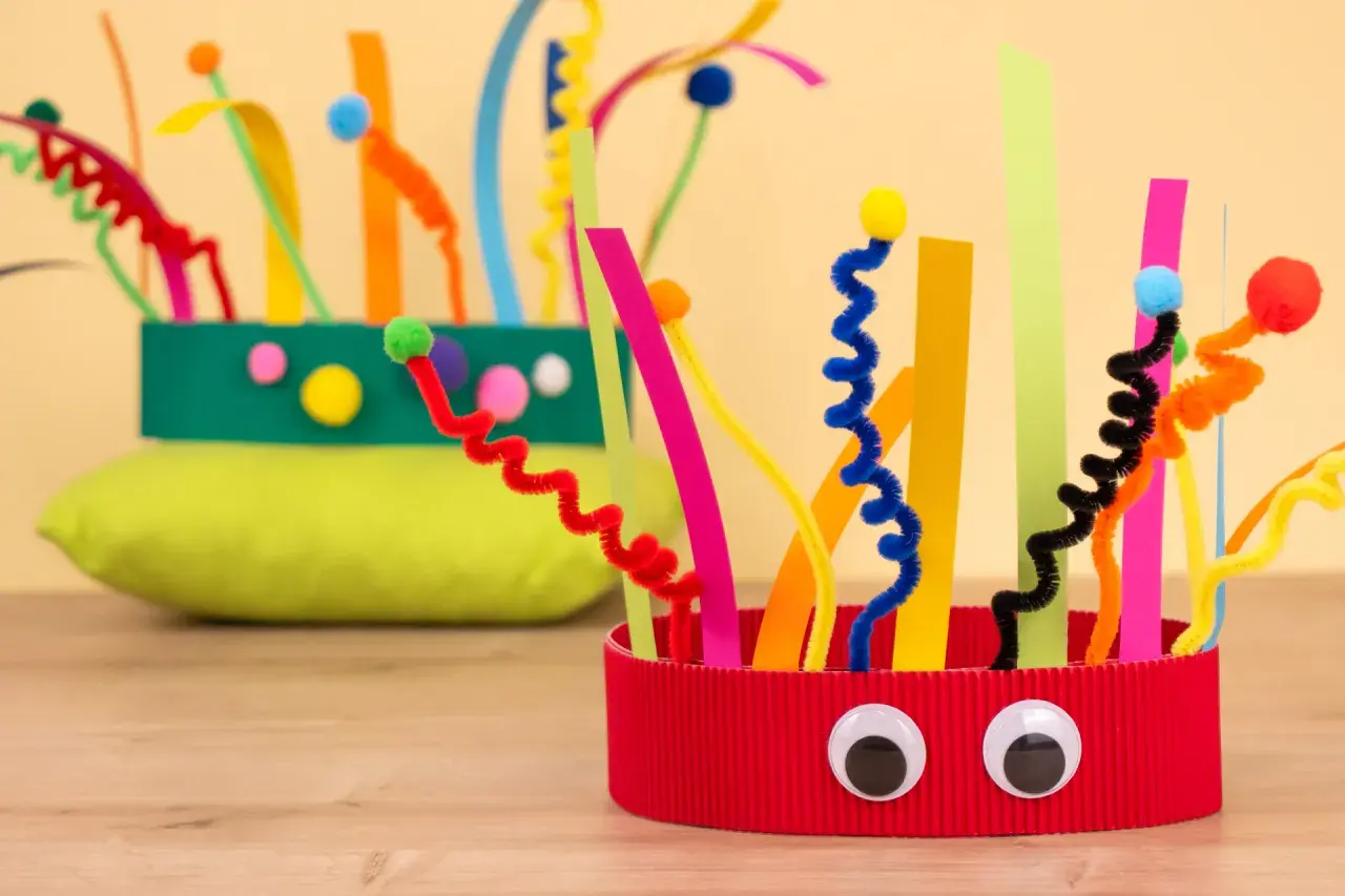 Bunte Faschingskrone, gebastelt mit Pfeifenreinigern und Papierstreifen. Ein lustiges Bastelprojekt für die Krippe.