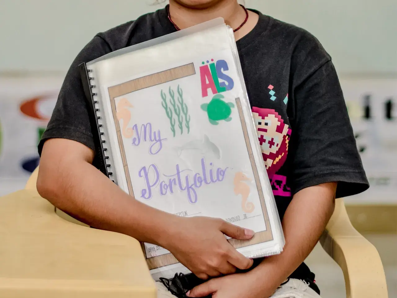 Ein Kind hält stolz sein **Portfolio Kindergarten** mit maritimen Motiven. Seepferdchen, Quallen und eine Schildkröte zieren die Mappe.