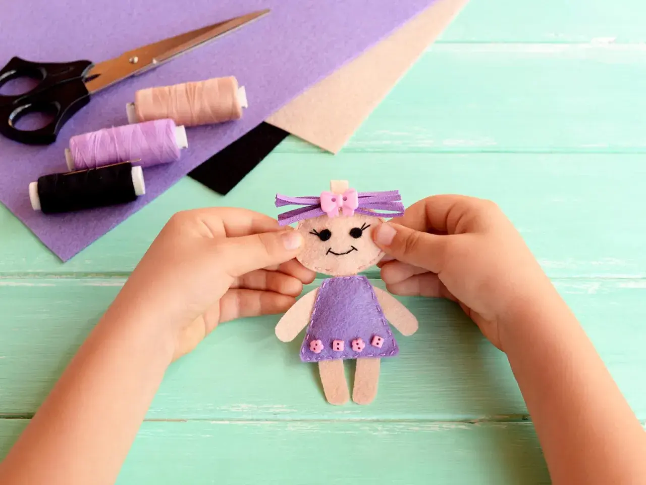 Kleine Hände basteln eine Filzpuppe. Schere, Faden und Filz liegen bereit für das Filzen mit Kindern.