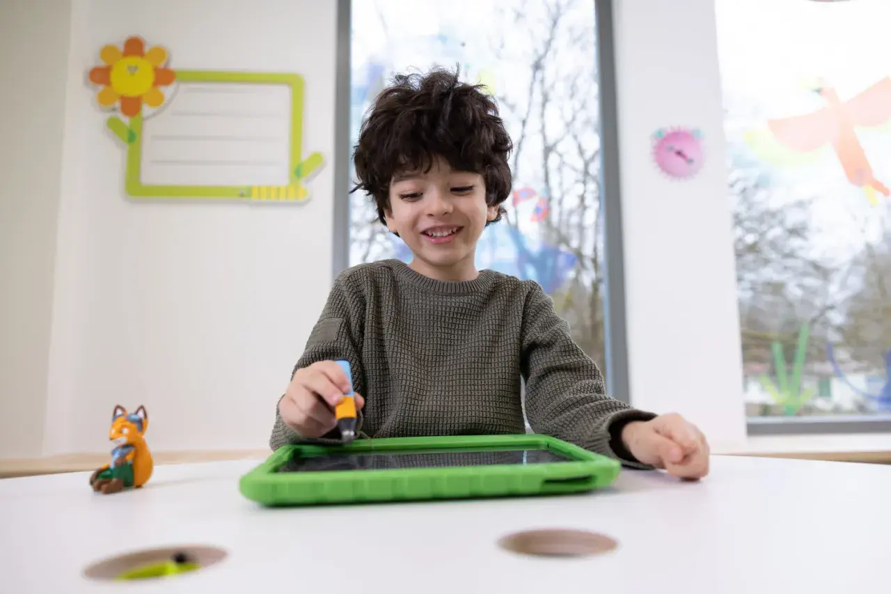 Ein Junge übt mit einem Stift auf einem Tablet, was eine spielerische Art ist, graphomotorische Fähigkeiten zu entwickeln.