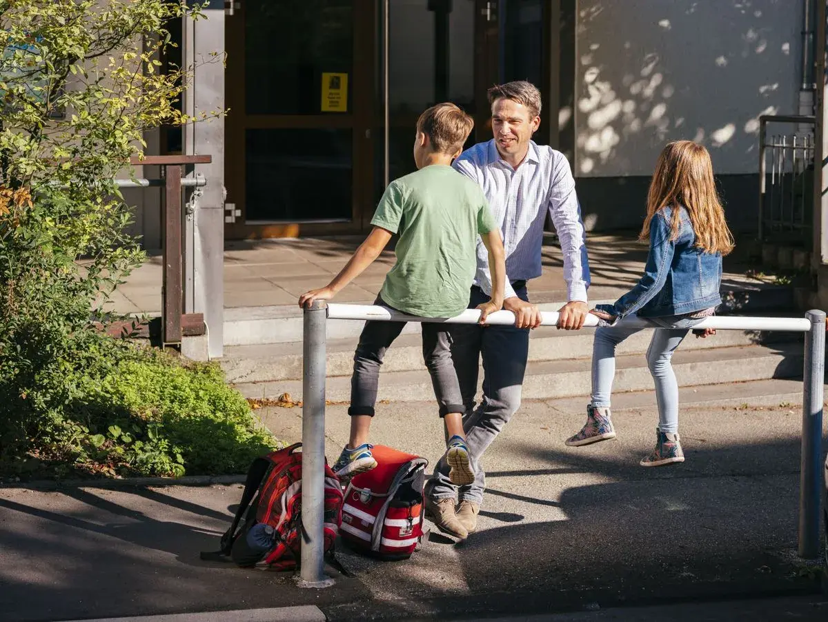 Ein Mann spricht mit zwei Kindern vor einer Schule. Vielleicht plant er, als lehrer bundesland wechseln.
