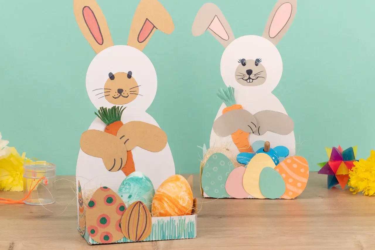 Zwei süße Osterhasen zum osterhase basteln halten Karotten. Bunte Ostereier liegen in Körbchen.