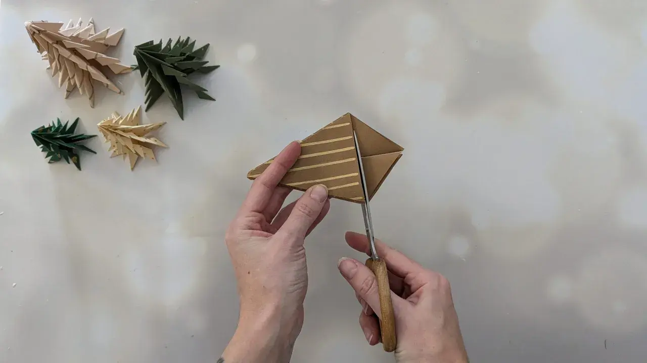 Schere schneidet Papier für einen Tannenbaum. Einfache Anleitung zum Falten von Tannenbäumen.