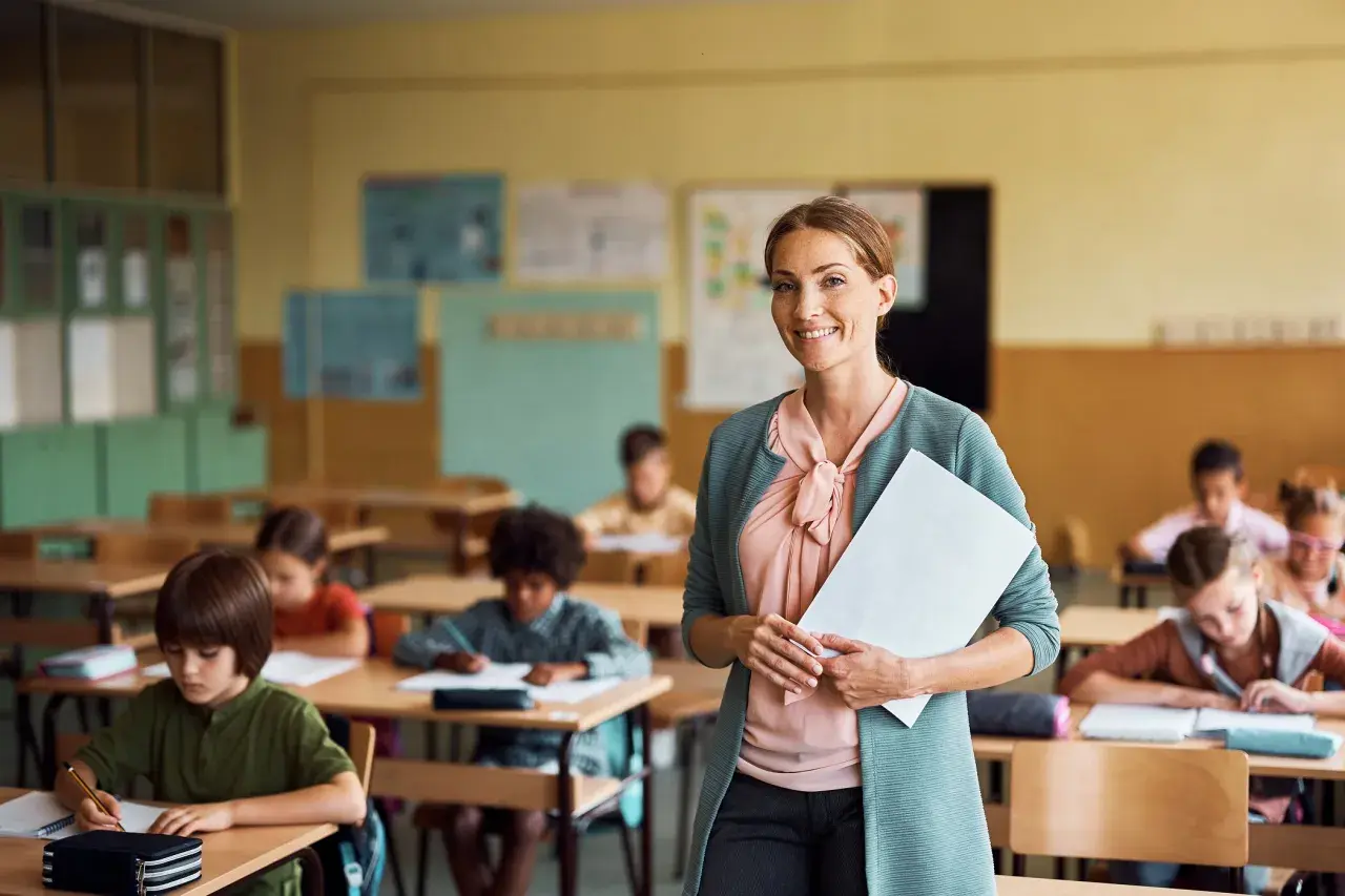 Lehrerberuf pro contra: Eine lächelnde Lehrerin mit Unterlagen steht vor einer Klasse voller konzentrierter Schüler.
