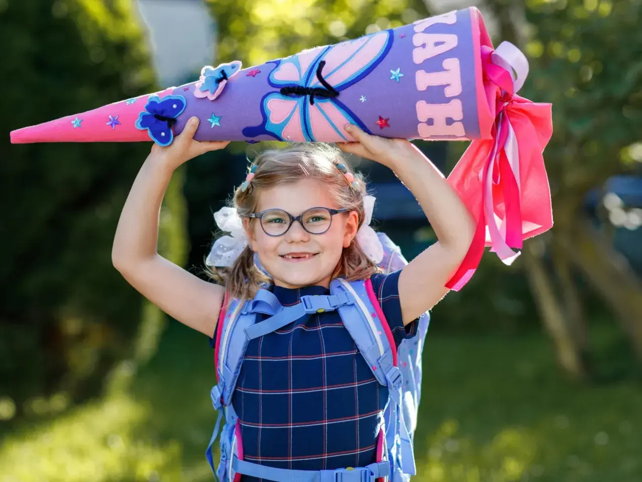 Ein Mädchen mit Schultüte und Rucksack, bereit für die erste Klasse Grundschule. Bunte Schmetterlinge zieren die Schultüte.