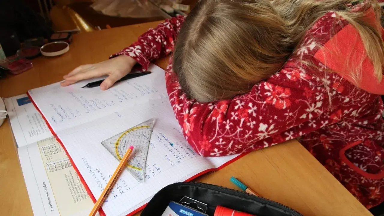 Müdes Kind mit Kopf auf dem Schreibtisch, umgeben von Schulbüchern und Stiften. Vielleicht helfen Ritalin Tabletten bei der Konzentration?